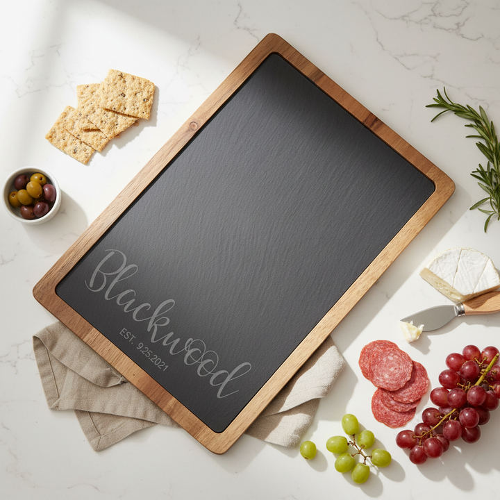 wood and slate charcuterie board with couples name and established date on a marble surface with food items.