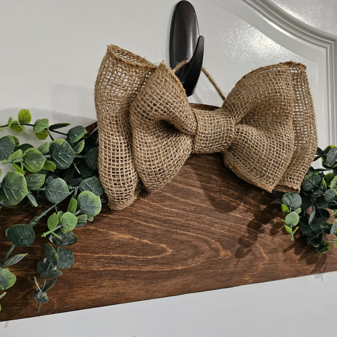 Wooden sign with a burlap bow and greenery on a white background