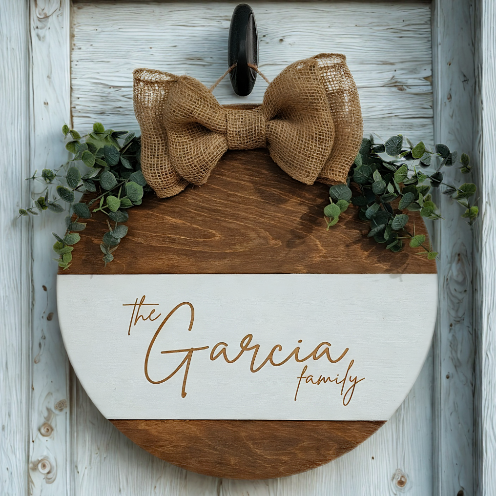Decorative sign with a burlap bow and greenery on a wooden background
