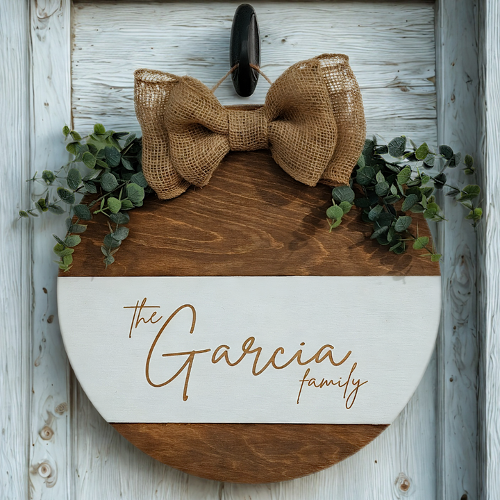 Decorative sign with a burlap bow and greenery on a wooden background