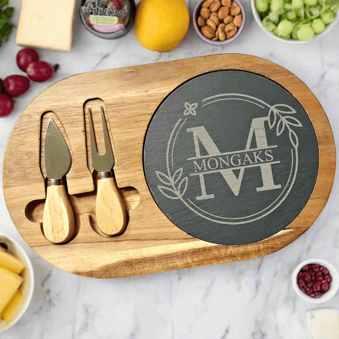 Wooden cheese board with engraved monogram and initial, two cheese knives, and a marble background with fruits and nuts.