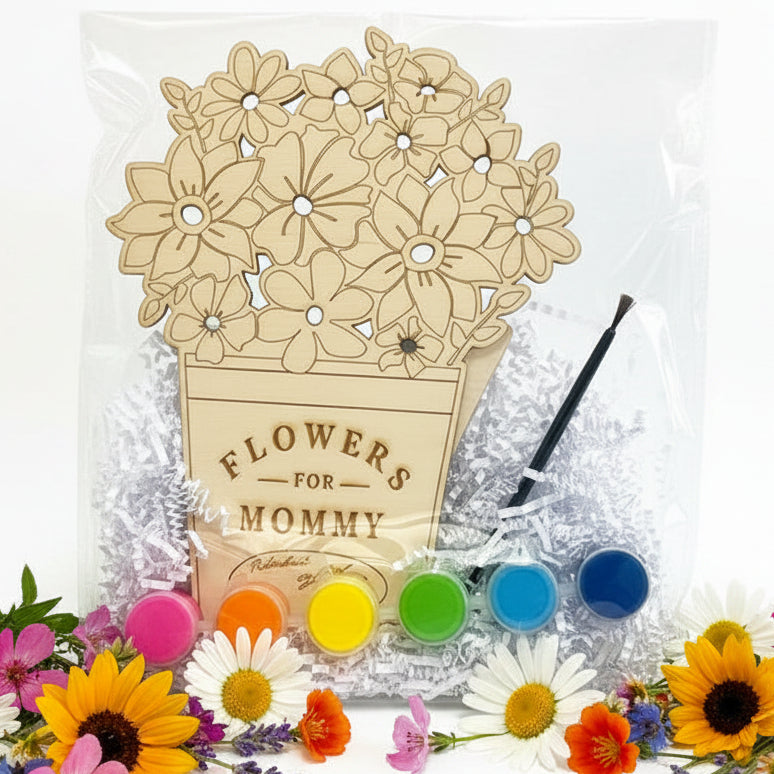 A floral flower-pot wood painting kit for Mommy, featuring a wooden pot and flower design, six small paint pots in pink, orange, yellow, green, light blue, and dark blue, a black paintbrush, and silver crinkle paper inside a clear plastic bag on a white background.