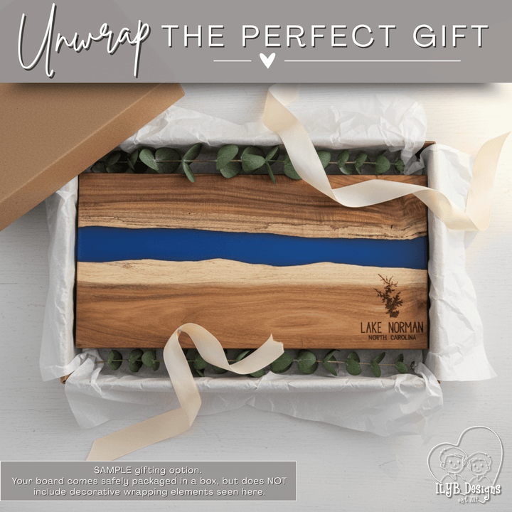 Acacia wood charcuterie board with blue resin inlay and 'Lake Norman North Carolina' text engraved in bottom right corner laying in a gift box
