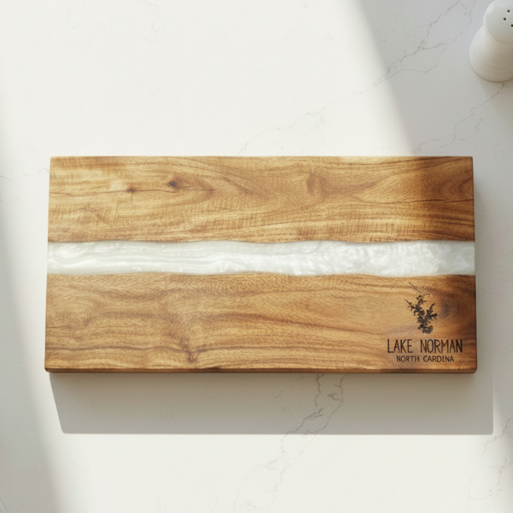 Wooden cutting board with a white resin center inlay on a marble surface, featuring 'Lake Norman North Carolina' engraving and silhouette of lake