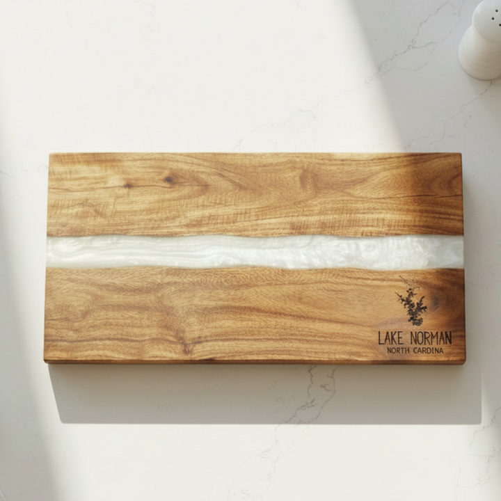 Wooden cutting board with a white resin center inlay on a marble surface, featuring 'Lake Norman North Carolina' engraving and silhouette of lake