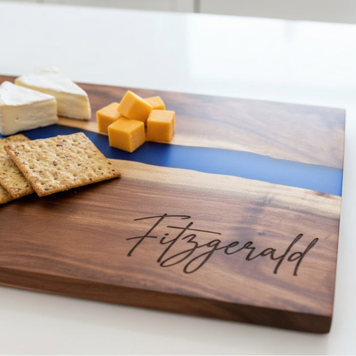 Wooden cutting board with cheese, crackers, and blue resin design, with name engraved in bottom right corner