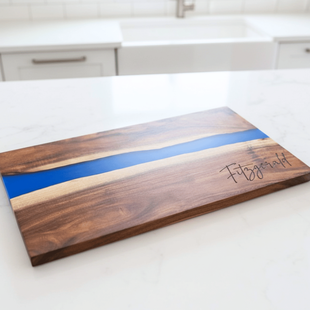 Wooden cutting board with blue resin inlay on a kitchen counter with a last name engraved in the bottom right corner
