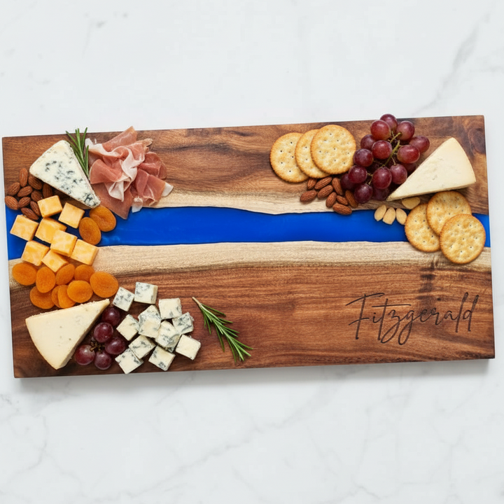 Wooden charcuterie board with engraved last name with assorted cheeses, fruits, and crackers on a white surface.