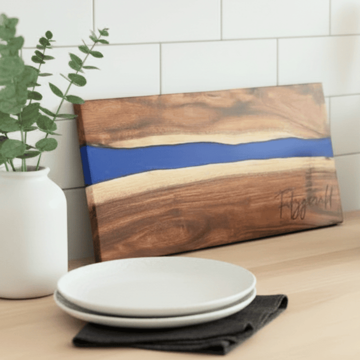 Wooden cutting board with blue resin inlay on a kitchen counter with plates and a plant.
