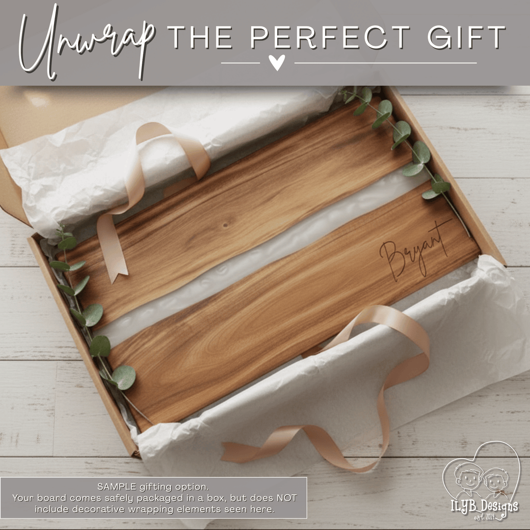 Wood charcuterie board with white resin inlay and name engraved in bottom right corner in an open gift box. Text on top of photo says 'unwrap the perfect gift'. Bottom text says 'Sample gift option. Your board comes safely packaged in a box, but does not include decorative wrapping elements seen here.'