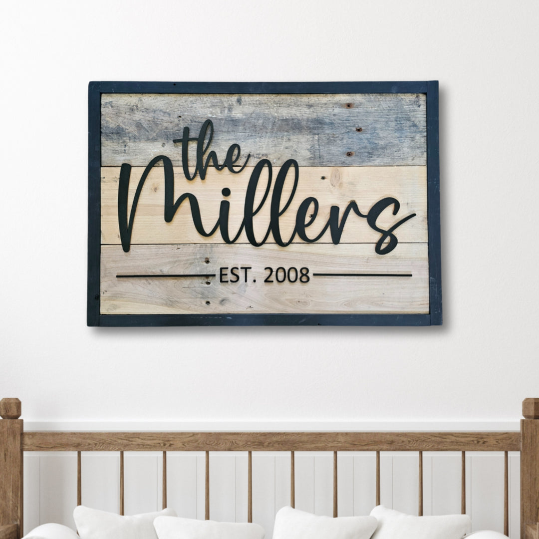 Wooden pallet sign with 'The Millers EST. 2008' on a white wall above a wooden bed frame.