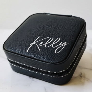 Black travel jewelry box with 'Kelly' engraving in metallic silver sitting on a marble surface
