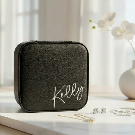 Black travel  jewelry case with 'Kelly' engraved in metallic silver sitting on a marble surface with jewelry items.