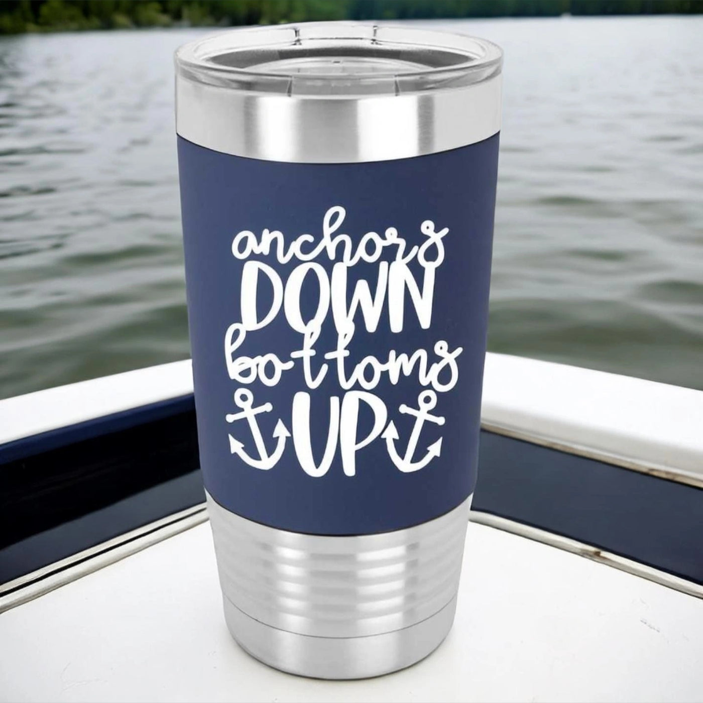 20 ounce stainless steel boat lover tumbler with navy silicone sleeve laser engraved in white and says Anchors Down Bottoms Up with an anchor on either side of the word up.