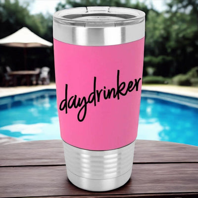 Stainless steel tumbler with pink silicone sleeve laser engraved in black with daydrinker at an angle across the tumbler. Funny drinking tumbler is sitting on a table in front of a pool.