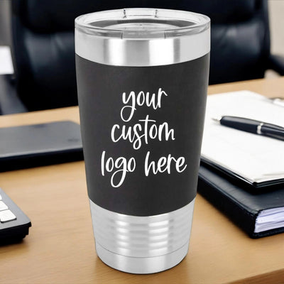 Black stainless steel custom branded tumbler sitting on a desk with a custom logo laser engraved in white on a black silicone sleeve.