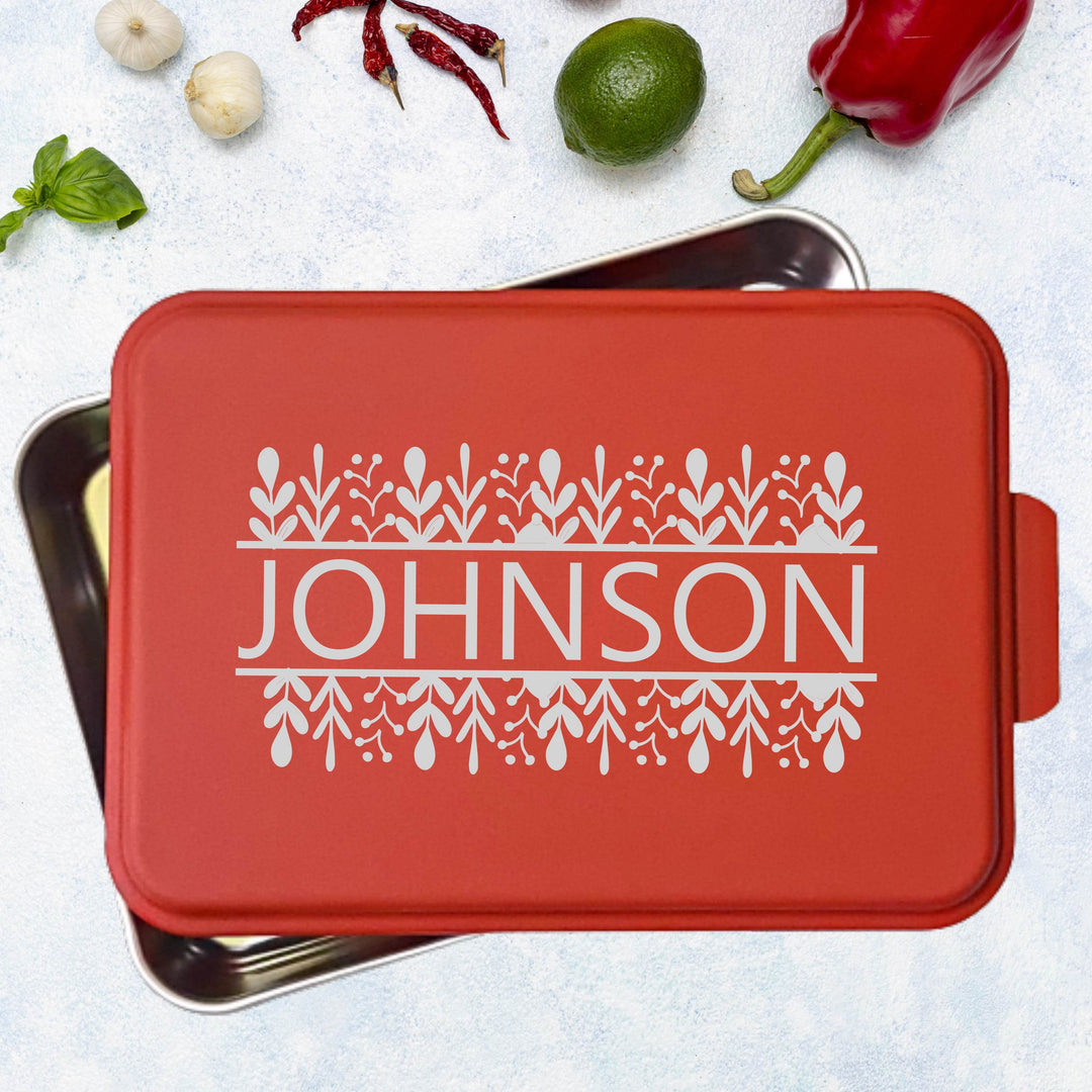 Metal cake pan with red lid personalized with family name 'Johnson' laser engraved on it, surrounded by kitchen items on a light surface.