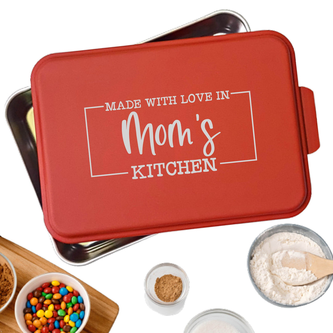 Personalized aluminum cake pan with red lid laser engraved with 'Made with Love in Mom's Kitchen' text, surrounded by baking ingredients on a white background