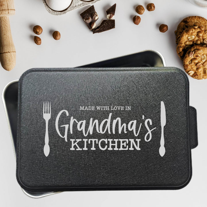 Aluminum cake pan with 'Made with love in Grandma's Kitchen' text laser engraved on a black powder coated lid on a white background with cookies and chocolate.