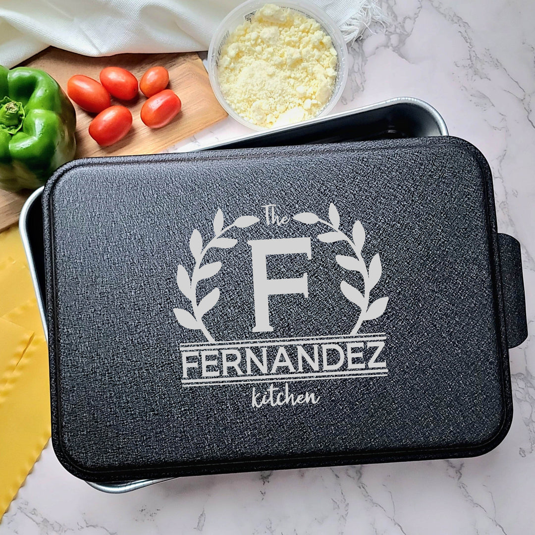 Aluminum rectangular baking pan personalized with 'Fernandez kitchen' engraved on black lid sitting on a marble surface with vegetables.