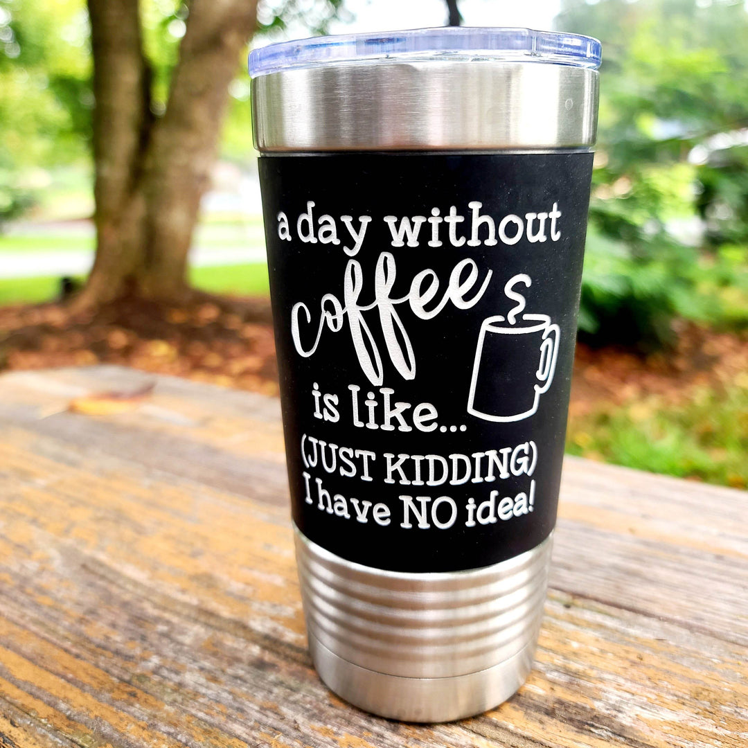 Black tumbler with humorous coffee quote 'a day without coffee is like...just kidding I have no idea' on a wooden surface outdoors