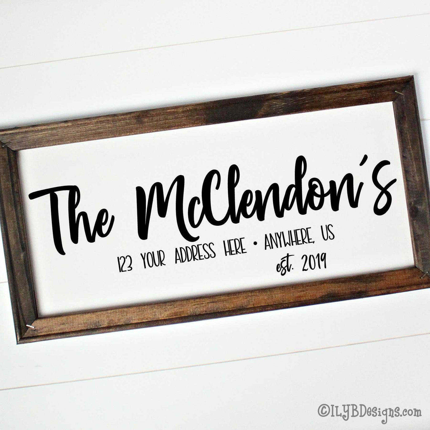 Dark walnut stained frame on a white canvas with a black design. Design is placed horizontally on the 20"x10" sign. Family name is in a bold script font with an optional address and established year underneath. 