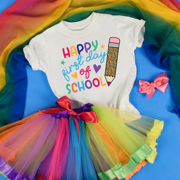 White youth back to school shirt with a whimsical, giant leopard print pencil perfectly complemented by rainbow-colored words that spell out Happy 1st Day of School. Shown paired with a rainbow tutu.