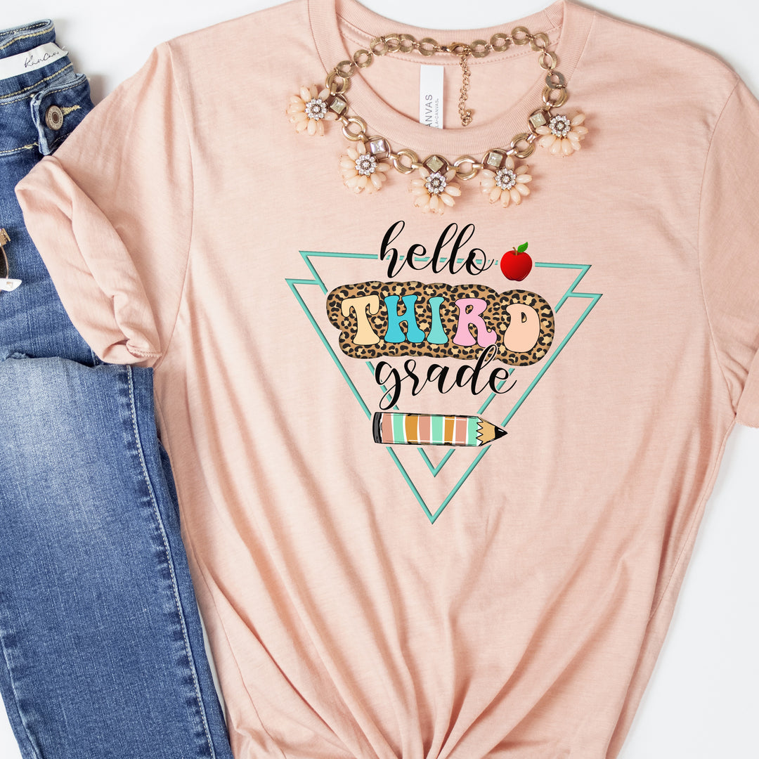 Heather peach color grade level team teacher shirt featuring colorful retro letters with leopard print behind them and says hello third grade along with a pencil and apple.