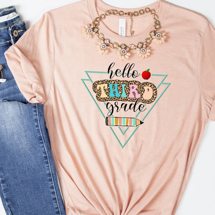 Heather peach color grade level team teacher shirt featuring colorful retro letters with leopard print behind them and says hello third grade along with a pencil and apple.