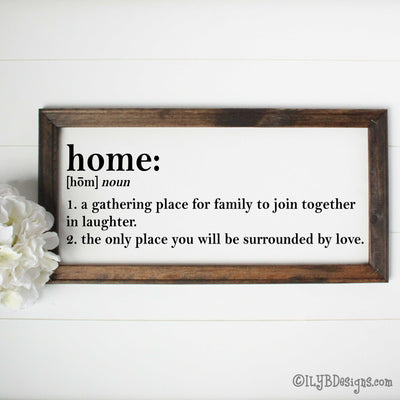 Dark walnut stained 20"x10" frame on a white canvas with black printed words that look like a dictionary definition.  It reads, "home: noun, 1. a gathering place for family to join together in laughter. 2. the only place you will be surrounded by love." Design is placed horizontally on the sign.