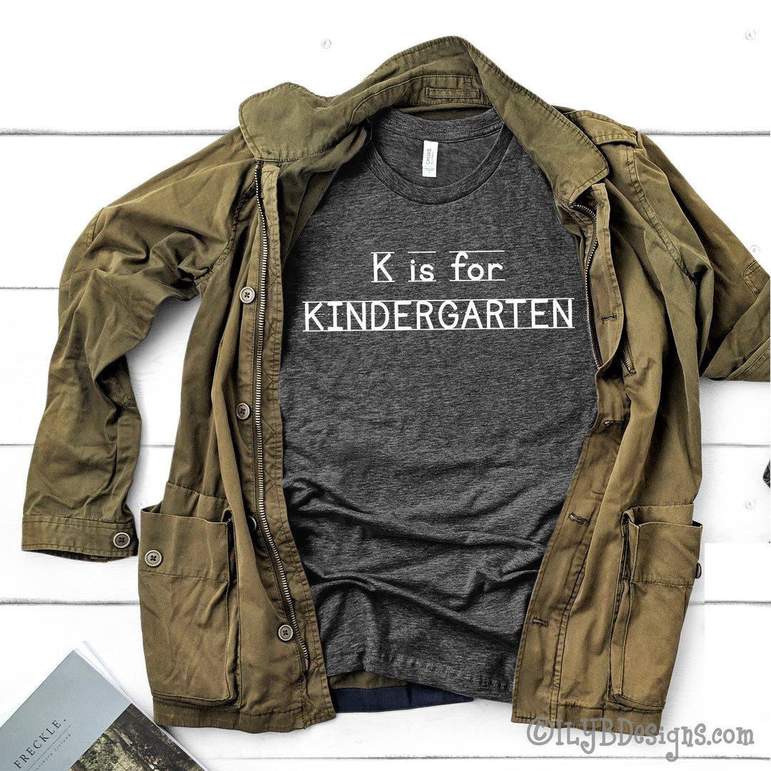 Dark gray heather kindergarten teacher shirt that says K is for Kindergarten in a white font that looks like primary lined writing paper.