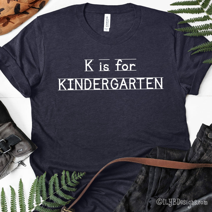 Heather navy kindergarten teacher shirt that says K is for Kindergarten in a white font that looks like primary lined writing paper.