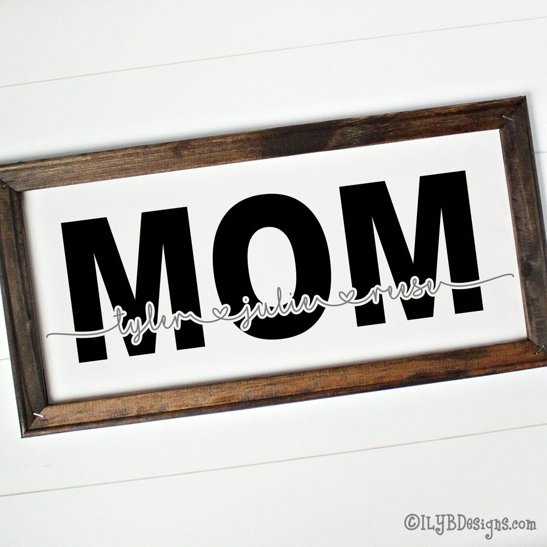 Wooden-framed canvas sign with 'MOM' in large black text and 3 childrens names connected with heart cut out of word mom in gray.