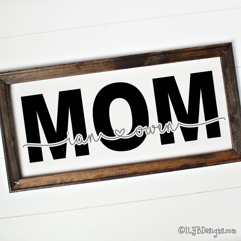 Wooden-framed canvas sign with 'MOM' in large black text and kids names connected with heart cut out of word mom in gray.
