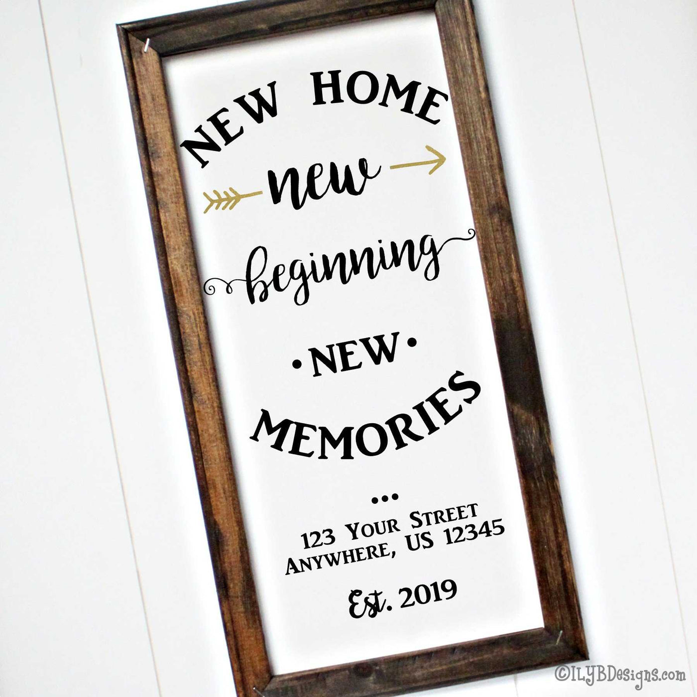 Dark walnut stained frame on a white canvas with black wording in various fonts that says, "New home, new beginning, new memories."  A metallic gold arrow is split on each side of the first "new." Under the saying is the option to add an address and an established year. 