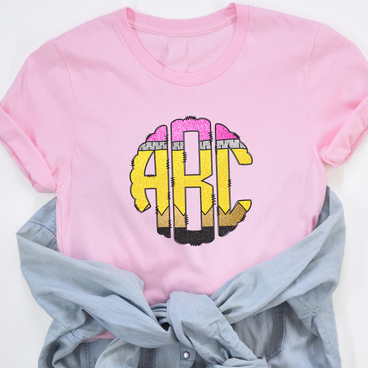Pink monogram school pencil shirt with round 3 letter monogram in the middle.  Each letter of the monogrammed shirt looks like a colorful school pencil.