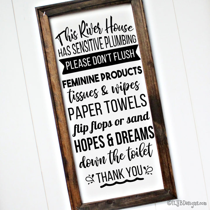 Dark walnut stained frame on a white canvas with a black design. The design is word art in various decorative fonts saying: This river house has sensitive plumbing. Please don't flush feminine products, tissues and wipes, paper towels, flip flops or sand, hopes and dreams down the toilet. Thank you. Sign measures 10"x20" and design is placed veritcally.