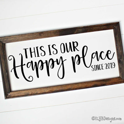 Dark walnut stained 20"x10" frame on a white canvas with black words in a mix of script and print fonts. It reads, "This Is Our Happy place since 2019." The design is placed horizontally on the sign.