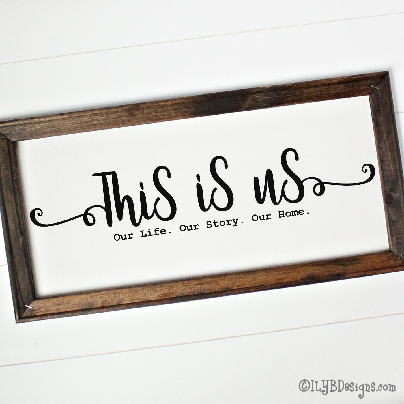 Dark walnut stained 20"x10" framed canvas with "This is us" in a black script font followed by a typewriter font that says, "Our Life. Our Story. Our Home." 