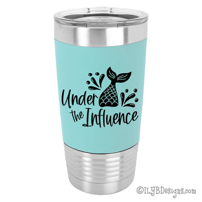 Under the Influence Mermaid Tail personalized 20oz stainless steel tumbler with teal silicone sleeve. Laser engraved in black is a mermaid tail splashing out of water with the words, "Under the Influence".
