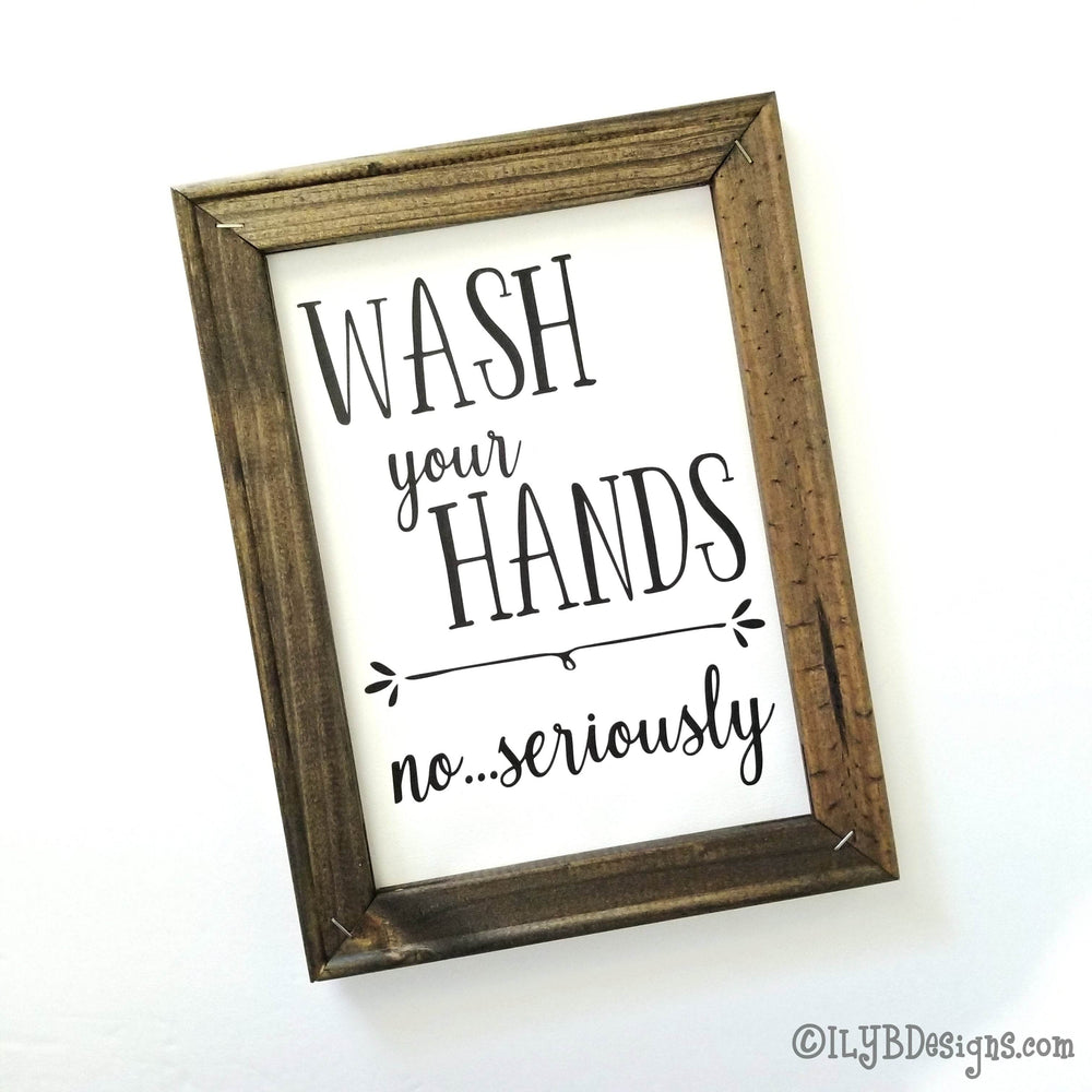 Framed canvas sign with 'Wash your hands no...seriously' black text on a white canvas background with a brown frame.