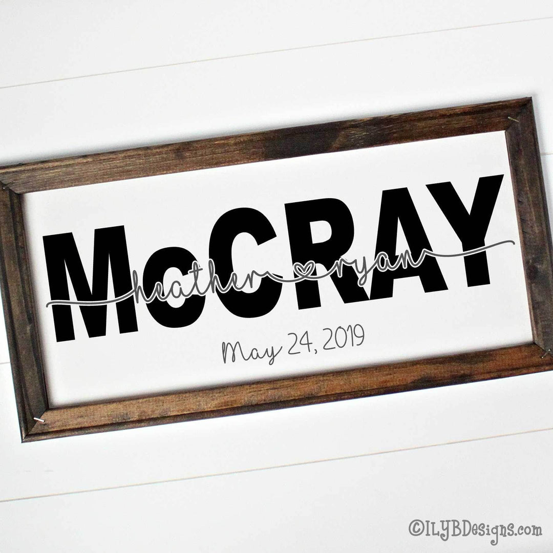 Wooden-framed sign with 'McCray' and  first names cutout of middle of last name and wedding date on a white canvas with a brown frame.